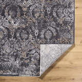 Close-up of the Alexei Area Rug, a machine-woven rug in black, charcoal, gray, and tan with a traditional floral pattern. Fold