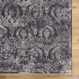 Close-up of the Alexei Area Rug. Traditional floral pattern in black, charcoal, gray, and tan on a wood floor. Corner