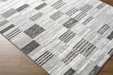 Close up of the Chiaki Light Gray Area Rug, featuring a geometric block and stripe pattern in ivory, light gray, and silver gray. Corner