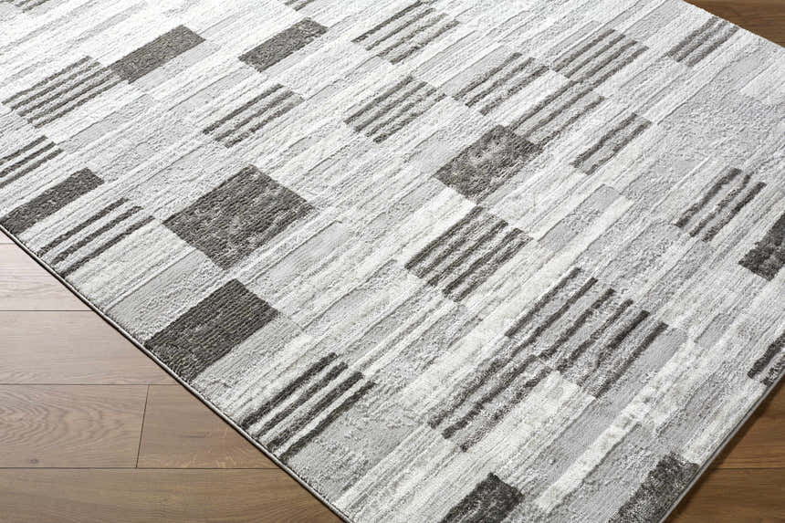 Close up of the Chiaki Light Gray Area Rug, featuring a geometric block and stripe pattern in ivory, light gray, and silver gray. Corner