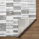 Close-up of the Chiaki Light Gray Area Rug showing its geometric pattern, texture, and backing on wood floor. Fold