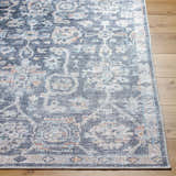 Close-up of the Eleni rug. Machine woven polyester rug in beige, black, burnt orange, denim, and gray on wood floor. Front