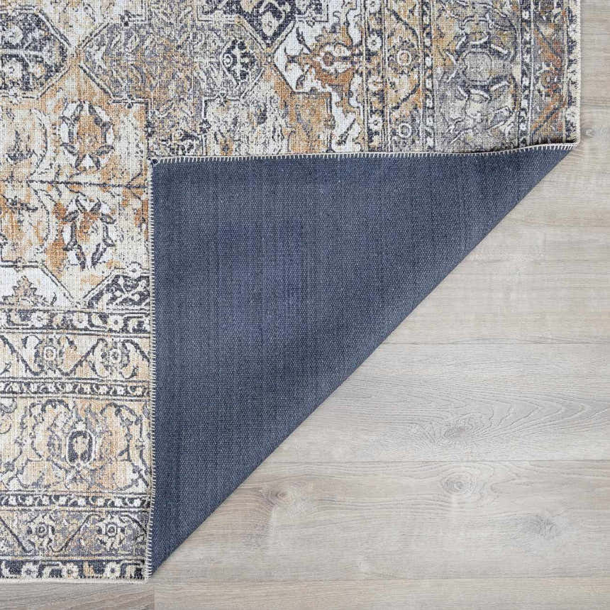 Close-up of the Dagatan Washable Area Rug showing beige, black, and camel oriental pattern and blue backing on light wood floor. Fold