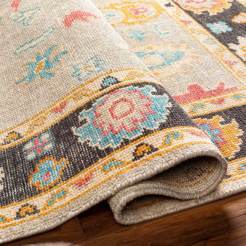 Close up of the hand-knotted Dalupaon Area Rug. Features a traditional floral pattern in black, beige, blue, pink, and mustard. Fold