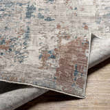Close-up of the Danlugan Area Rug showing its charcoal, cream, brown, and blue contemporary pattern and machine-woven texture. Fold