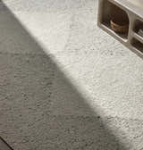 Close up of Ethara Ivory Charcoal rug showing wool texture and global pattern next to a light wood media console. Styleshot