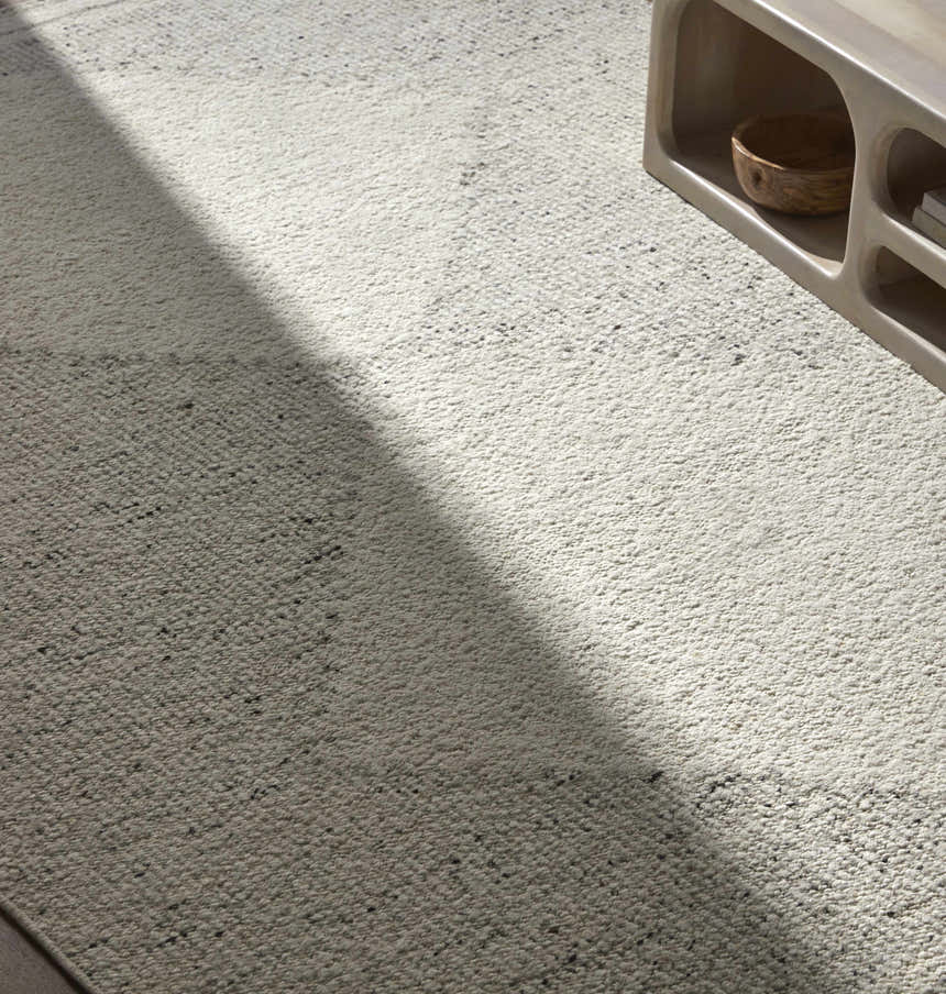Close up of Ethara Ivory Charcoal rug showing wool texture and global pattern next to a light wood media console. Styleshot