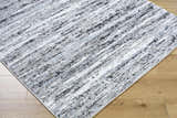 Close-up of the Azmina Area Rug. Contemporary design in black, ivory, light blue, and gray. Machine woven texture. Corner