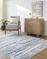 Living room scene with the Azmina Area Rug in black, ivory, and light blue, styled with a gray chair and wood cabinet. Roomscene-Rectangle
