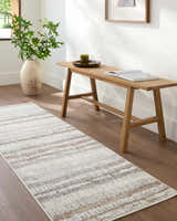 Hallway scene with a brown wood bench and the Asmara Brown Area Rug in ash, pearl, and sage colors. Styleshot