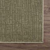 Close-up of the Leanna Green Washable Area Rug. The rug has a textured, geometric pattern in shades of gray-green. Corner