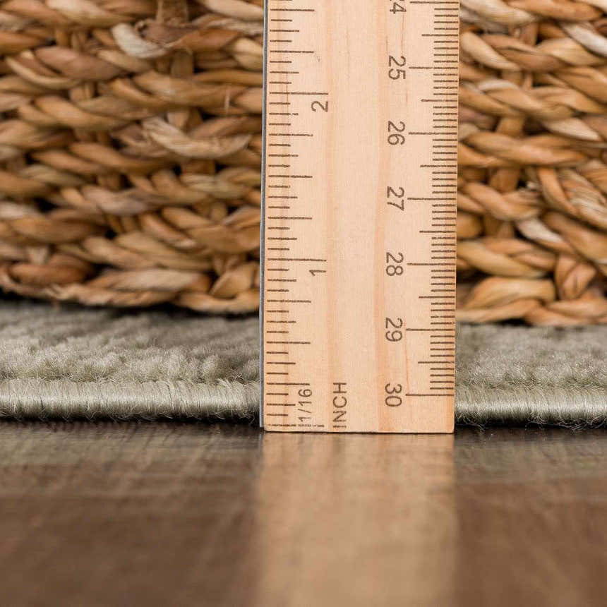 Close-up of the Leanna Green Washable Area Rug showing pile height with a ruler on a wood floor next to a woven basket. Pile
