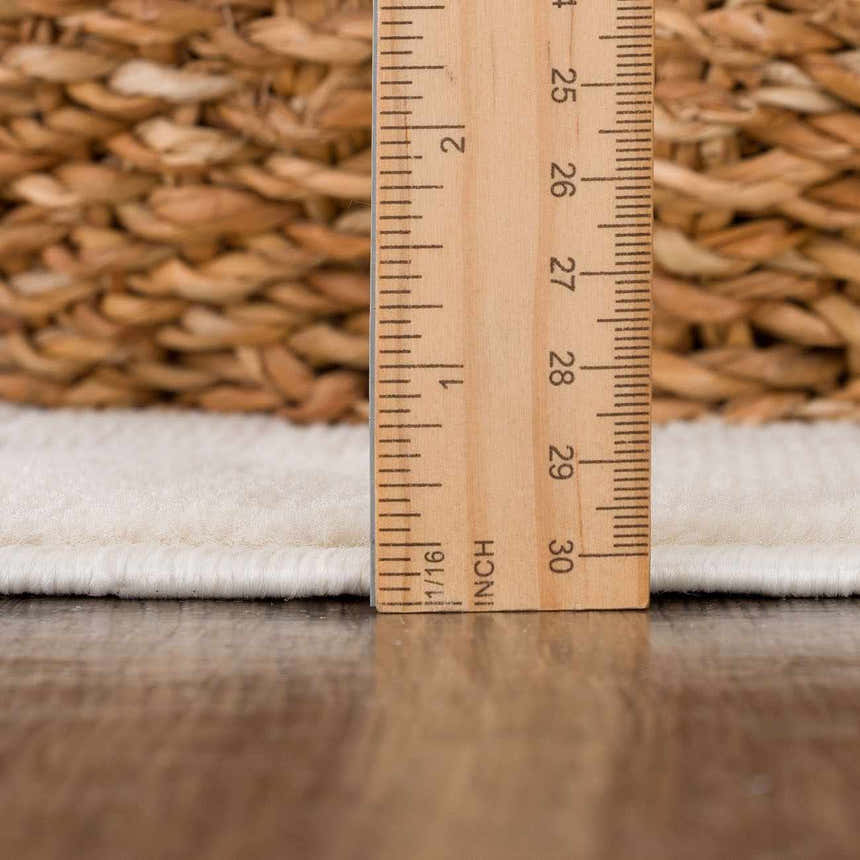 Close-up of Gaiwan Cream Washable Area Rug pile height, with wood ruler and woven basket in background. Pile