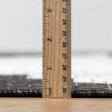 Close-up of the New Djugun Area Rug showing its pile height with a ruler. Black, charcoal, and off-white tones. Pile