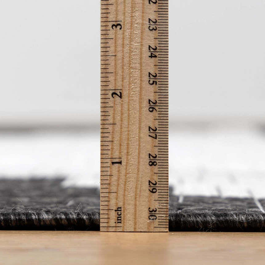 Close-up of the New Djugun Area Rug showing its pile height with a ruler. Black, charcoal, and off-white tones. Pile