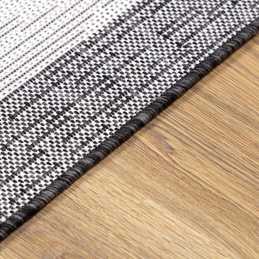Close-up of the Djugun Area Rug showing the black, charcoal, and off-white geometric pattern and woven texture. Pile