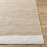 Close-up of the hand-woven Aderyn Jute Area Rug in camel, pearl, and tan on wood flooring. Natural fiber texture. Front