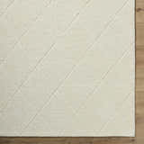 Close-up of the Almeda Washable Wool Area Rug in off-white, featuring a subtle diamond pattern and hand-tufted texture. Corner