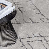 Close-up of the Flintville Moroccan Shag Area Rug, showing its charcoal geometric pattern and soft, light beige shag texture. Styleshot