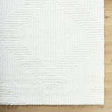 Close-up of the plush, cream Ashlyn White Area Rug featuring a subtle geometric shag pattern on a light wood floor. Corner