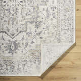 Close-up of the Alissa Cream Area Rug showing its traditional charcoal, gray, and tan floral pattern and folded corner. Fold