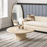 Living room scene with a striped Geographe Indoor Outdoor Rug, round coffee table, and cream sofa. Styleshot