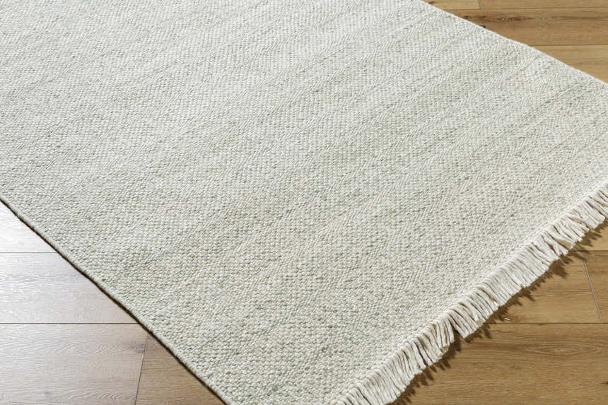 Close-up of the Sorell Sage rug. Textured weave in ecru, ivory, and sage. Wool rug with fringe detail. Corner