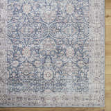 Close-up of the Mary Machine Woven Vivir x LIVABLISS rug. Features beige, black, red, and brown traditional floral patterns. Corner