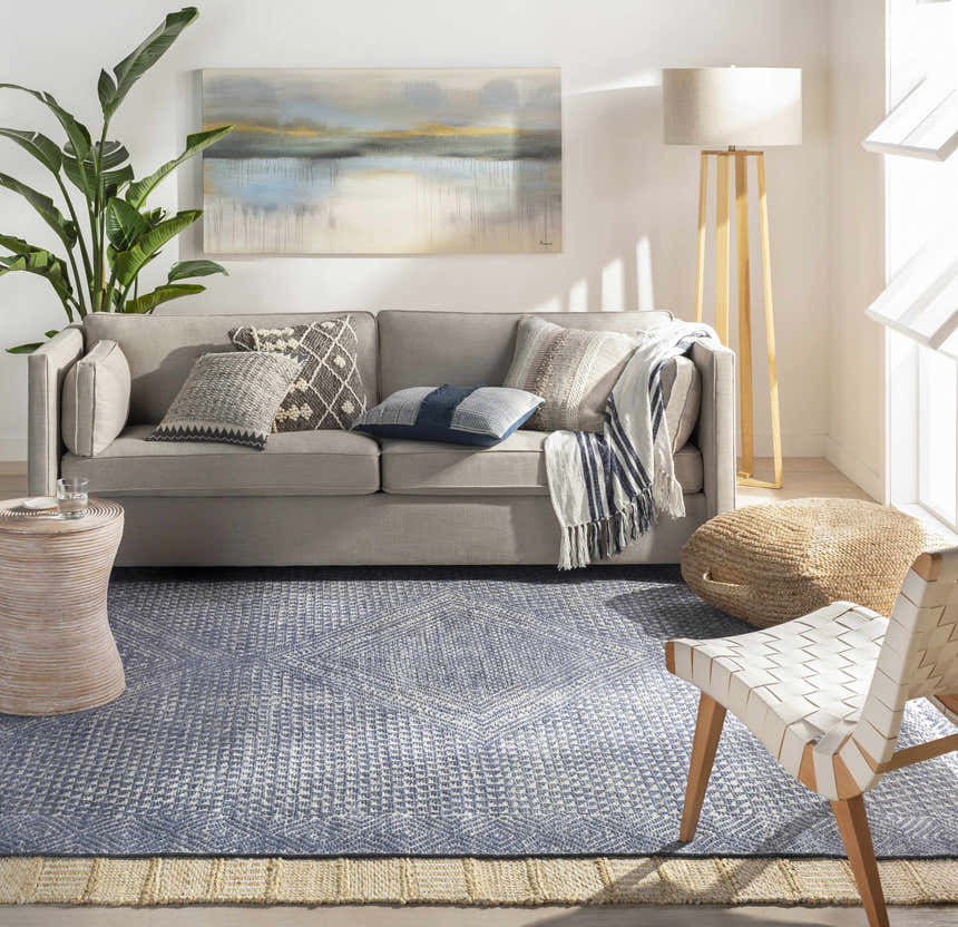 Living room scene with a beige sofa and the Bywong Area Rug in blue and jute, layered over a larger jute rug. Roomscene-Rectangle