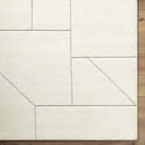 Close-up of the Alaina Area Rug. Ivory wool rug with a geometric charcoal line pattern. Hand-tufted texture. Corner