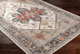 Close-up of a Halayhayin Premium Rug. Bohemian style rug in brick red, brown, cream, and gray on a dark wood floor. Corner