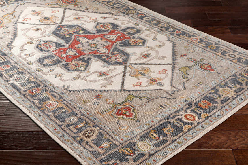 Close-up of a Halayhayin Premium Rug. Bohemian style rug in brick red, brown, cream, and gray on a dark wood floor. Corner