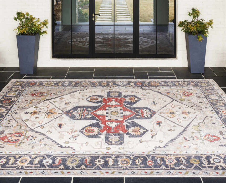 Entryway scene with a brick red and cream Halayhayin Premium Rug on black tile. Tall planters flank the glass door. Roomscene-Rectangle