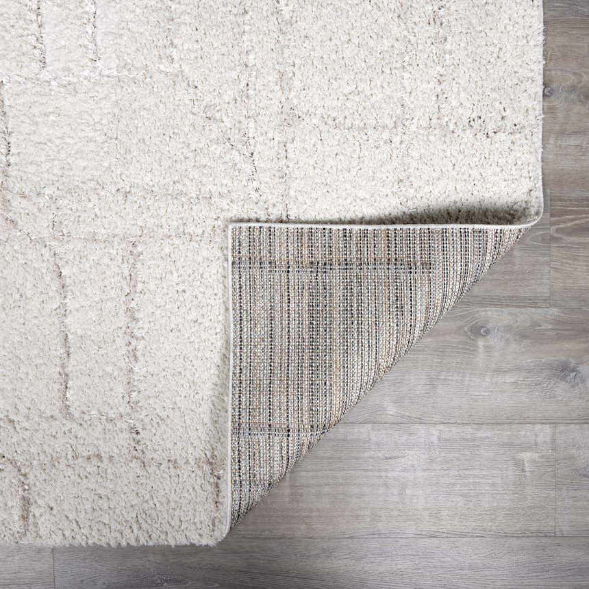 Close-up of the plush, cream Andia Grid Rug showing geometric shag design and rug backing. Fold