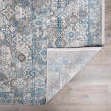 Close-up of the Hartsel Area Rug. Charcoal, dark blue, and gray traditional pattern with a folded corner showing the backing. Fold