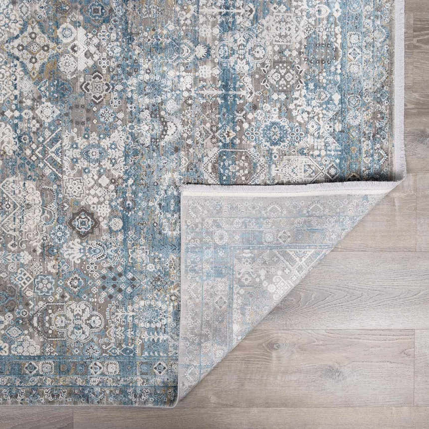 Close-up of the Hartsel Area Rug. Charcoal, dark blue, and gray traditional pattern with a folded corner showing the backing. Fold