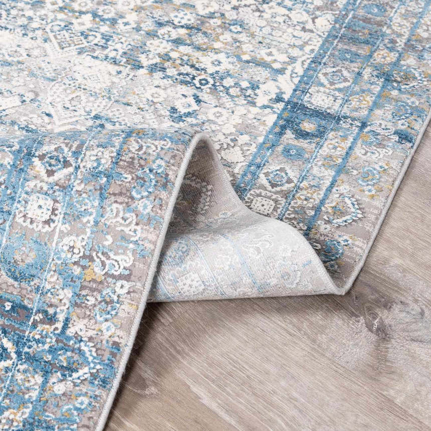 Close-up of the Hartsel Area Rug showing its blue, gray, and white traditional pattern and soft texture. Fold