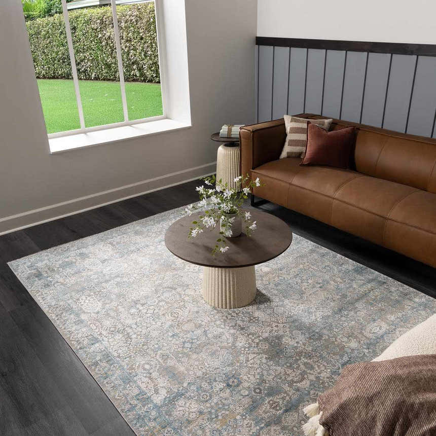 Living room scene with a blue and gray Hartsel Area Rug, brown leather sofa, and round coffee table. Roomscene-Rectangle