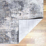 Close-up of the Ironwood Textured Luxe Rug. Charcoal, gray, light gray, brown, and taupe tones create a contemporary pattern. Fold