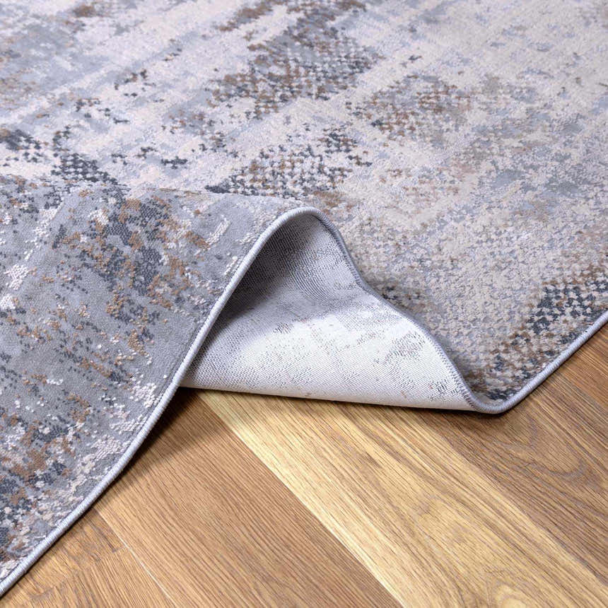 Close-up of the Ironwood Textured Luxe Rug showing its charcoal, gray, and brown abstract pattern and woven construction. Fold