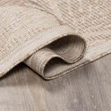 Close-up of the cream and tan Jens Area Rug showing its woven texture and bound edge detail on a gray wood floor. Fold