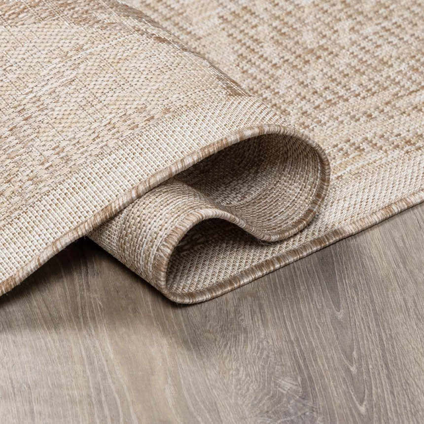 Close-up of the cream and tan Jens Area Rug showing its woven texture and bound edge detail on a gray wood floor. Fold