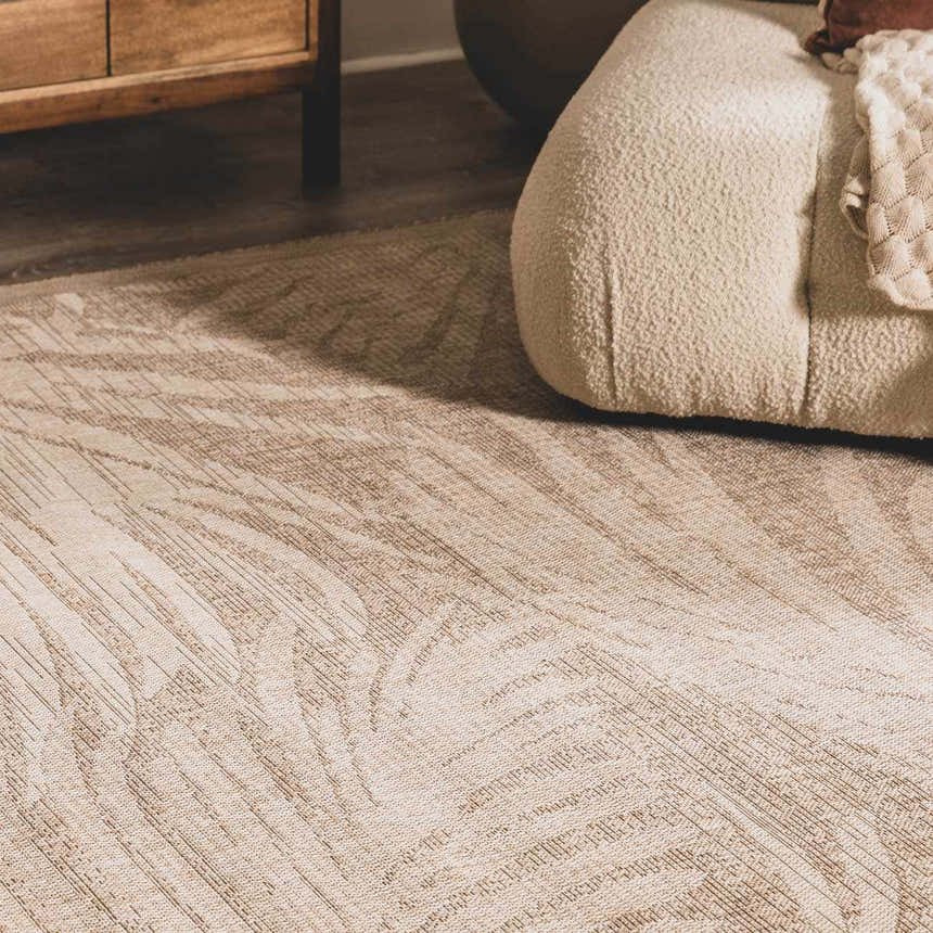 Close-up of the Jens Area Rug showing its cream and tan abstract pattern and machine-woven texture near a cream boucle chair. Styleshot