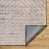 Close-up of the Tavran Taupe rug showing subtle linear texture, beige tones, and hand-loomed construction on a wood floor. Fold