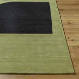 Close up of the Arvok Olive Green rug showing its charcoal block design, hand-tufted wool texture, and olive border on wood floors. Front