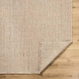 Close-up of the Cilaa Modern Hand Woven Wool Area Rug showing its neutral color, woven texture, and fringed edge on wood floor. Fold