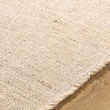 Close up of the textured, hand woven Cilaa Modern Wool Rug in a neutral beige color on wood flooring. Texture