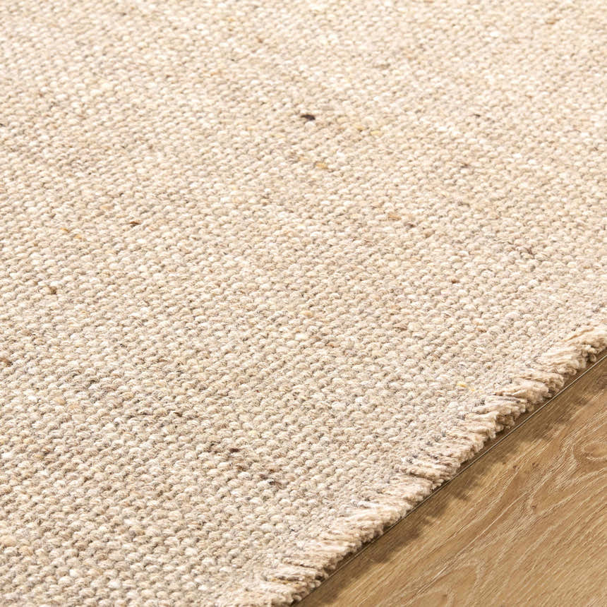 Close up of the textured, hand woven Cilaa Modern Wool Rug in a neutral beige color on wood flooring. Texture