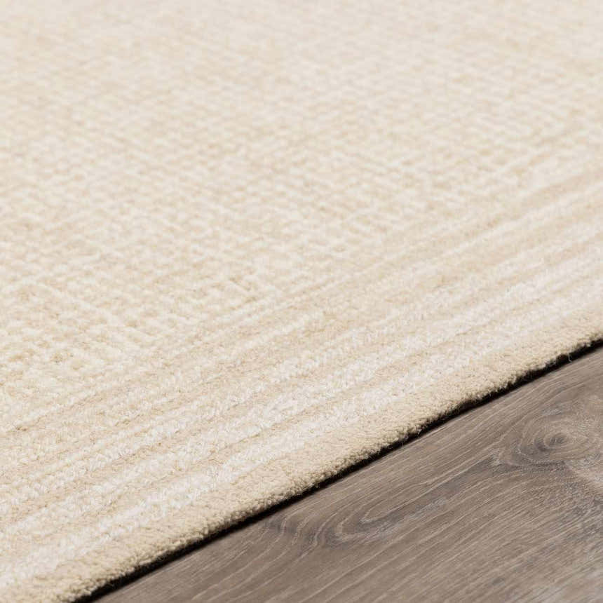 Close up of the hand-tufted Kayoko Ivory Area Rug showing its subtle pattern and texture on dark wood flooring. Pile