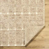 Close-up of the hand-woven Keegan Area Rug. Beige, sandstone, and taupe wool rug with a textured, dotted pattern. Fold